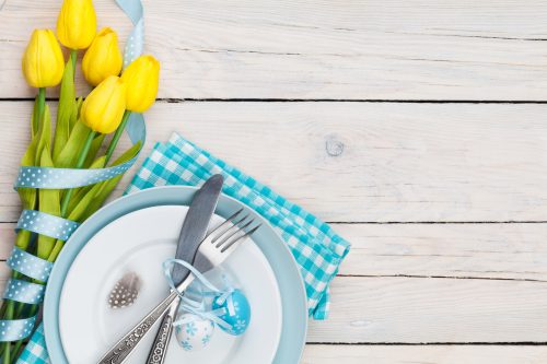Easter with yellow tulips and colorful eggs over white wooden table. Top view with copy space